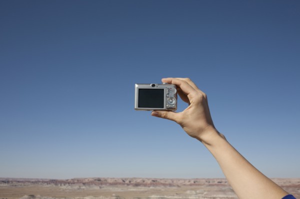 Hand of woman holding camera up against blue sky. Photo: Winslow Productions
