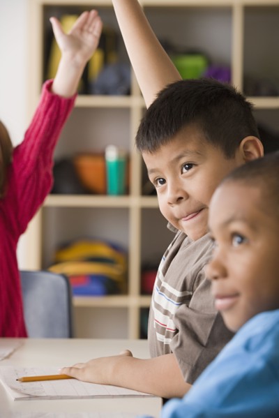 Children (6-7) raising hands in classroom. Photo : Rob Lewine