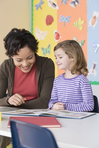 Teacher helping girl (6-7) in reading. Photo : Rob Lewine
