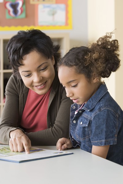 Teacher helping girl (6-7) to read. Photo : Rob Lewine