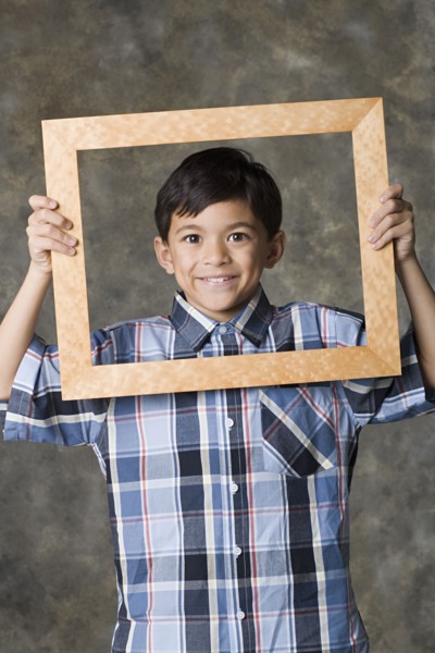 Portrait of smiling boy (8-9) looking through frame, studio shot. Photo : Rob Lewine