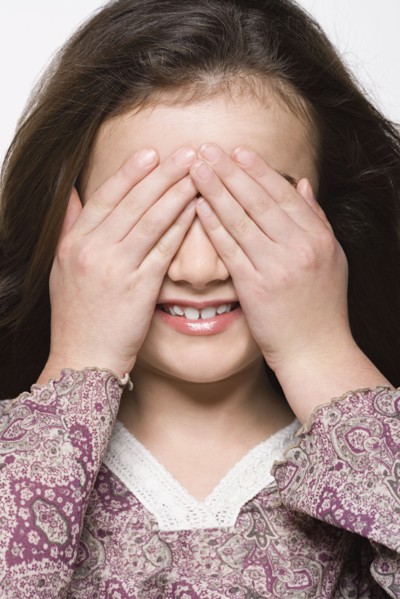 Smiling girl (8-9) covering her eyes, studio shot. Photo : Rob Lewine