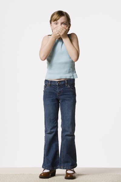 Smiling girl (8-9) covering her mouth, studio shot. Photo: Rob Lewine