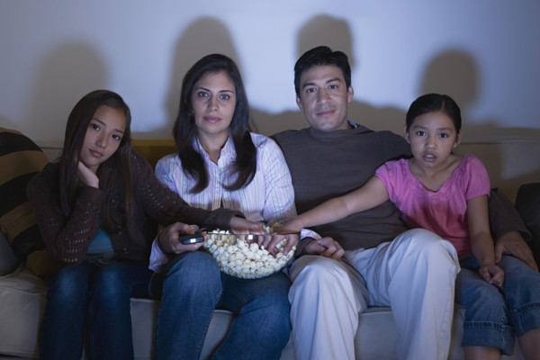 Family with two daughters (8-9, 10-11) watching tv on sofa. Photo : Rob Lewine