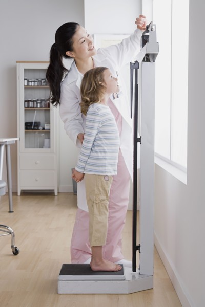 Female doctor measuring girl's (4-5) weight. Photo: Rob Lewine