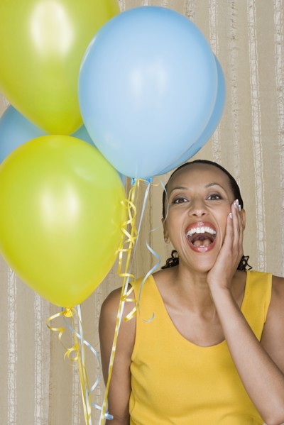 Happy mid adult african woman shouting while holding yellow and blue balloons. Photo: Rob Lewine