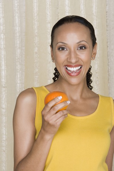 Portrait of smiling woman holding orange, studio shot. Photo : Rob Lewine