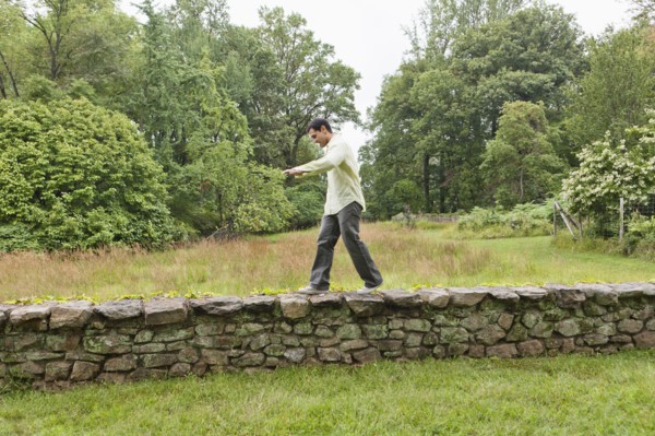 USA, New Jersey, Man walking on stone wall on field. Photo : Tetra Images