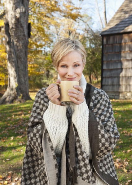Portrait of smiling woman holding mug in front of cottage house in Autumn. Photo: Tetra Images