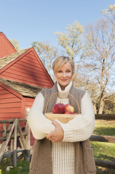 USA, New Jersey, Portrait of smiling woman holding basket with apples in front of cottage house in