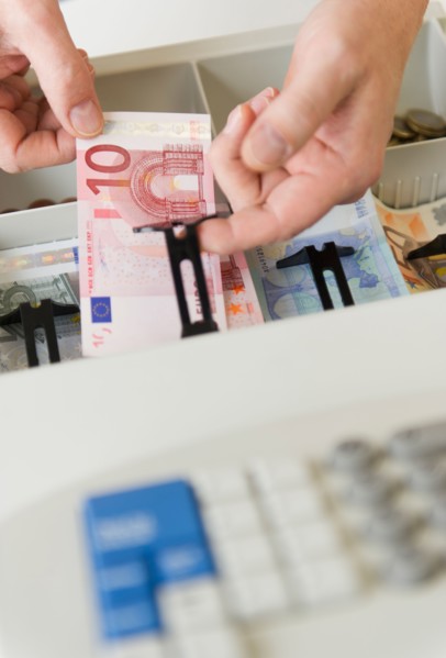 Close up of man's hand putting banknotes into cash register, studio shot.