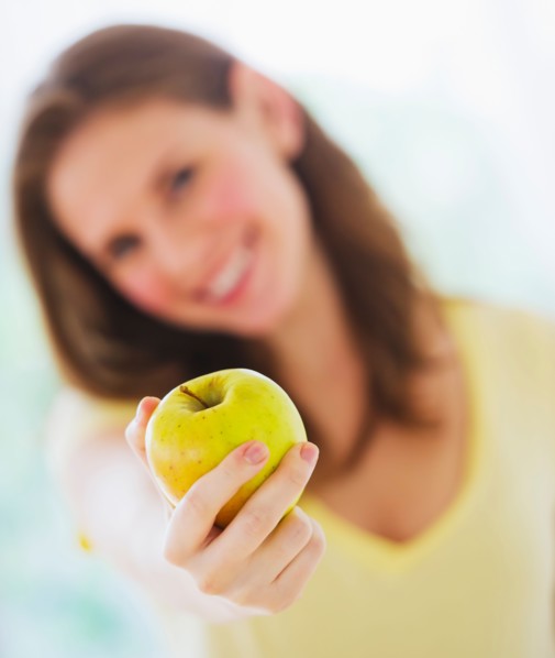 Smiling young woman holding apple. Photo : Daniel Grill