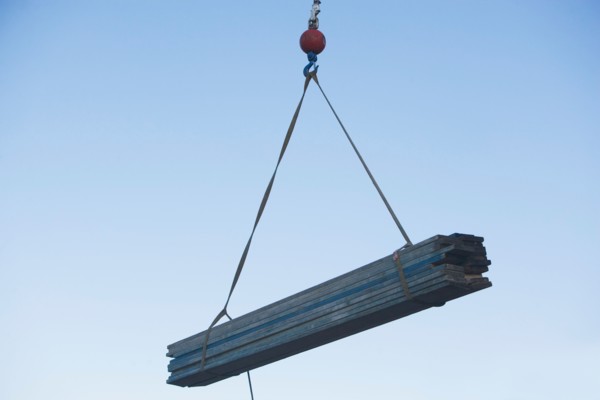 Mid-air view at crane's hook lifting wooden planks. Photo : fotog