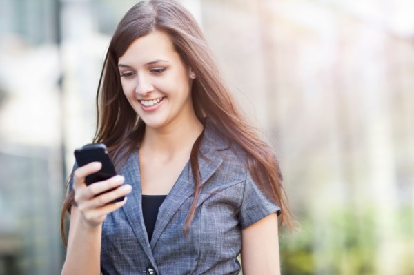 Young elegant woman standing and using mobile phone. Photo : Take A Pix Media