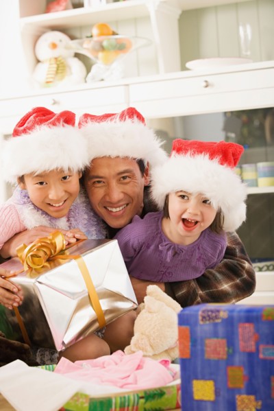 Portrait of father with two daughters (10-11) wearing Santa hats. Photo : Rob Lewine