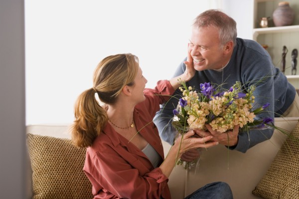 Senior man giving flowers to woman sitting on sofa. Photo : Rob Lewine
