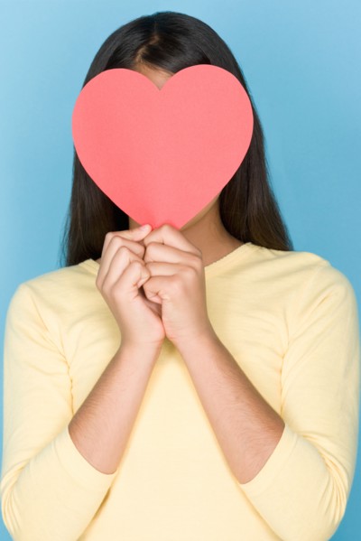 Studio portrait of teenage (16-17) girl holding paper heart over face. Photo : Rob Lewine