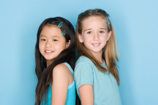 Studio shot portrait of two teenage girls standing back to back, head and shoulders. Photo : Rob