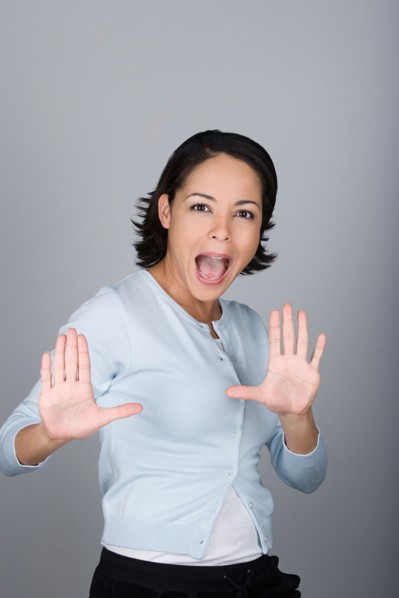 Studio shot portrait of mid adult woman with arms raised and open mouth, waist up. Photo : Rob