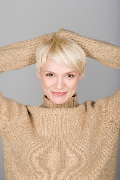 Studio shot portrait of mid adult woman with hands behind head, head and shoulders. Photo : Rob
