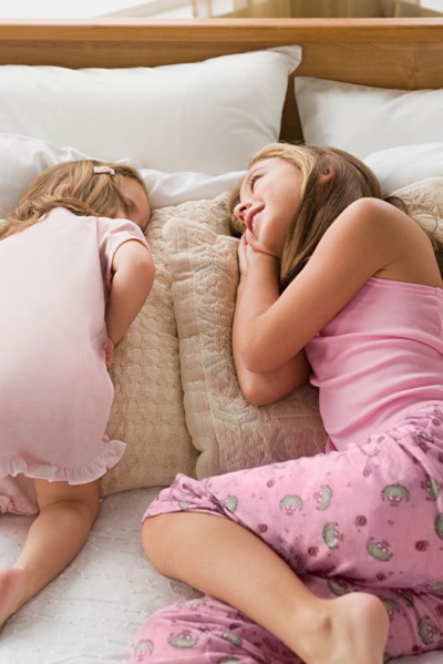 Sisters (8-9, 12-13) lying together on bed. Photo : Rob Lewine