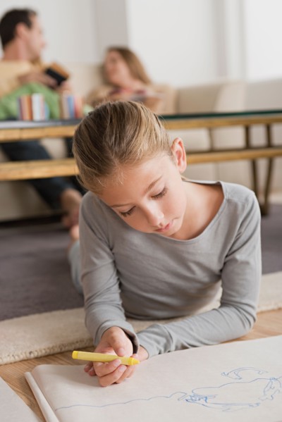 Girl (12-13) drawing in living room, parents in background. Photo : Rob Lewine
