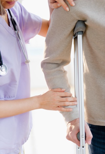 Close up of female doctor helping patient with crutch. Photo : Jamie Grill