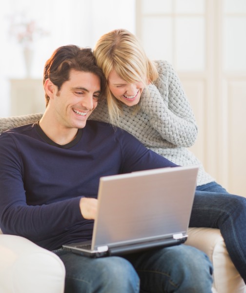 Happy couple sitting together on armchair and using laptop . Photo : Daniel Grill
