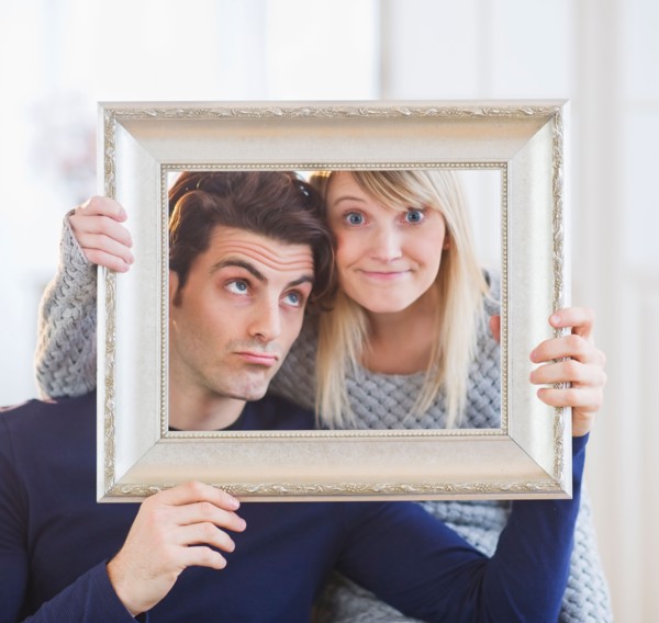Couple holding picture frame and making faces. Photo : Daniel Grill