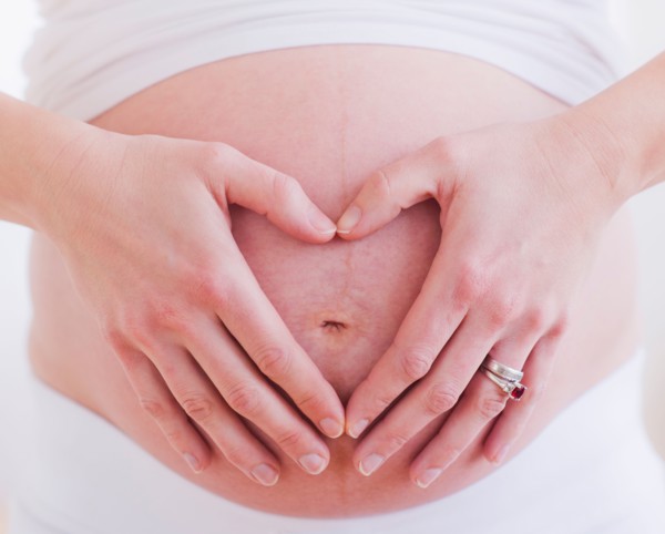 Pregnant woman with hands folded as heart on her belly. Photo : Daniel Grill