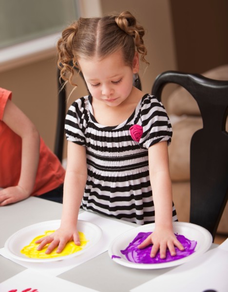 Girl (4-5) holding her hands on plates with paint. Photo : Mike Kemp