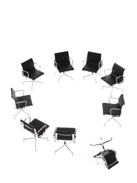 Corporate chairs forming circle on white background, one upside down. Photo : David Arky