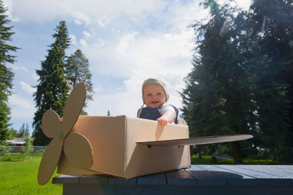 Baby boy (12-17 months) playing inside paper aeroplane made of cardboard box . Photo : Noah Clayton