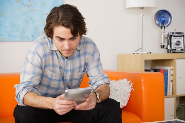 Young man sitting on sofa and using digital tablet. Photo : Rob Lewine