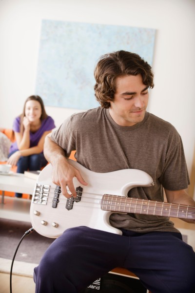 Young man playing electric guitar, young woman in background. Photo : Rob Lewine