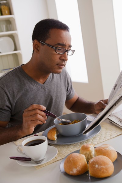 Mature man eating breakfast and reading newspaper. Photo : Rob Lewine