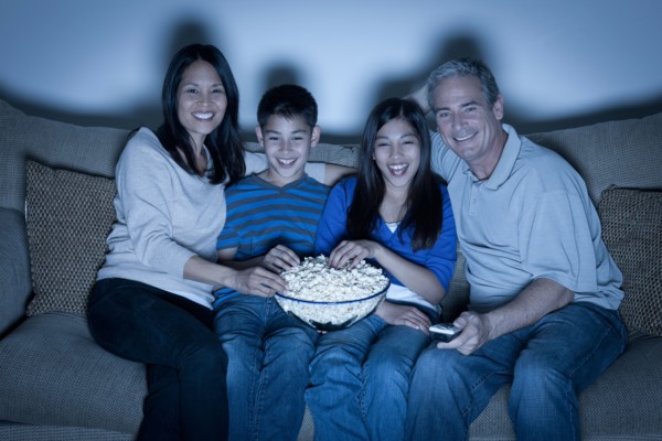Family sitting on sofa and watching television. Photo : Rob Lewine
