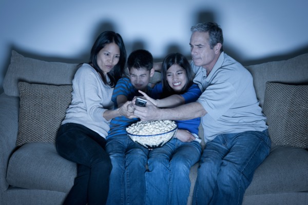 Family sitting on sofa and watching television. Photo : Rob Lewine