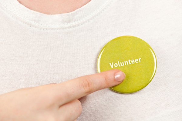 Close-up studio shot female hand pointing at yellow volunteer badge. Photo : Elena Elisseeva