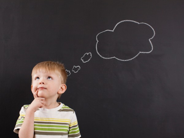 Cute toddler boy (2-3) standing against blackboard with thought bubble written in chalk. Photo :