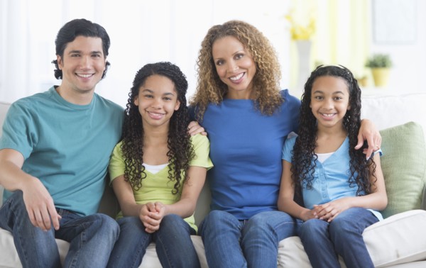 Portrait of parents with daughters (10-13) sitting on sofa.