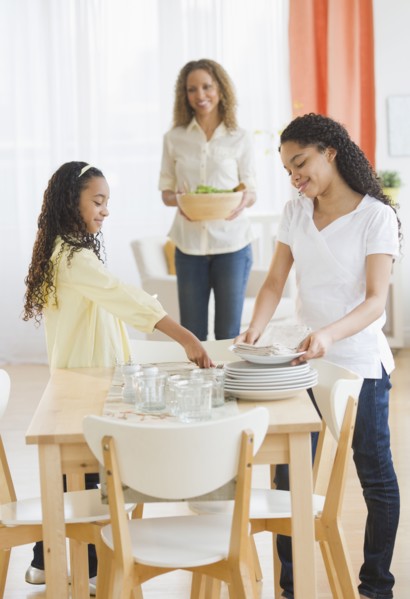 Mother with daughters (10-13) setting table.