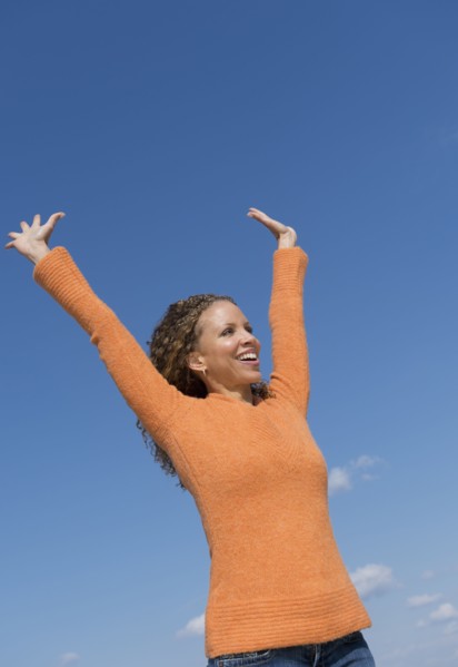 Mature woman with arms raised towards blue sky.