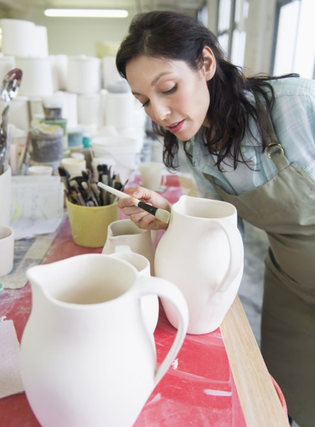 Female artist decorating pottery in studio.