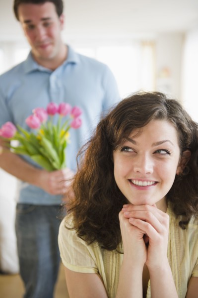 Woman smiling, man with flowers in background. 
Photo : Jamie Grill