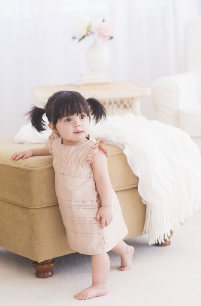Portrait of baby girl (12-17 months) standing near sofa. 
Photo : Daniel Grill