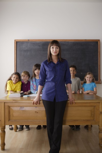 Teacher standing by desk with group of pupils. 
Photo : Rob Lewine