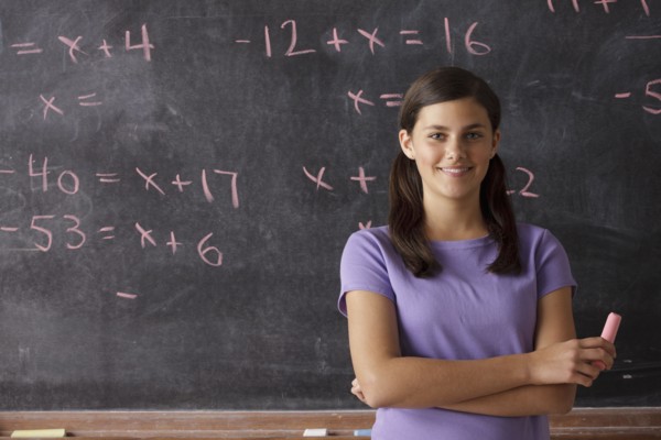 Portrait of schoolgirl (12-13) standing in front of blackboard during math classes. 
Photo: Rob