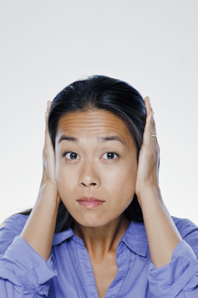 Portrait of young woman with hands covering ears, studio shot. 
Photo : Rob Lewine