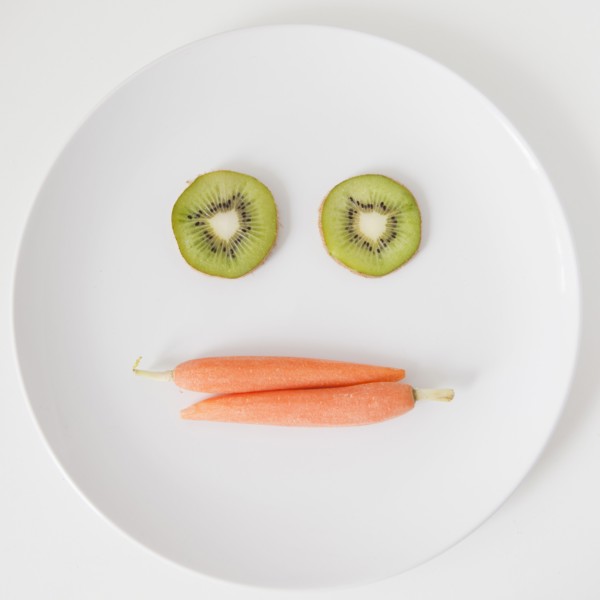 Fruit and vegetable face on plate, studio shot. 
Photo: Jessica Peterson